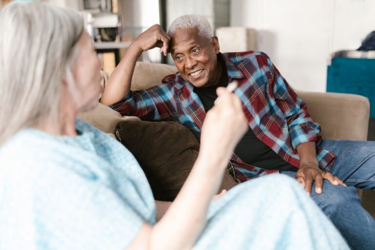 Black main in blue and red plaid sitting on couch smiling at his wife